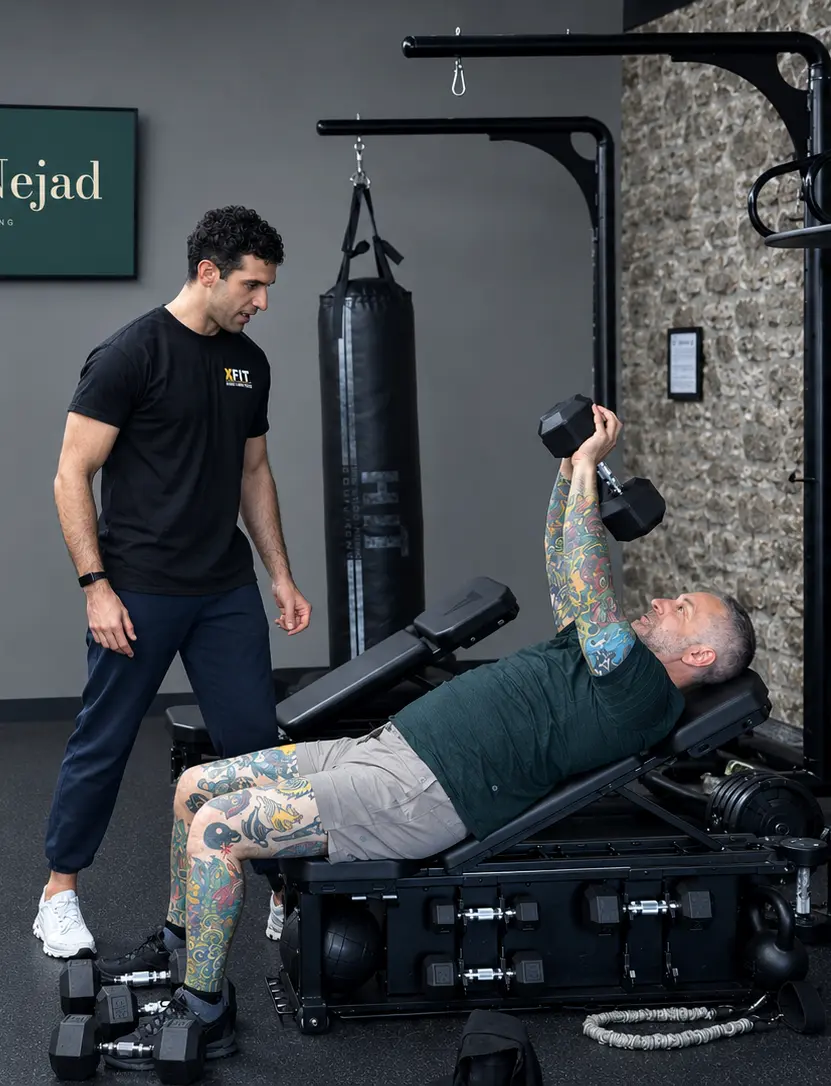 Sash Nejad coaching a client through a dumbbell press at his Montreal training space